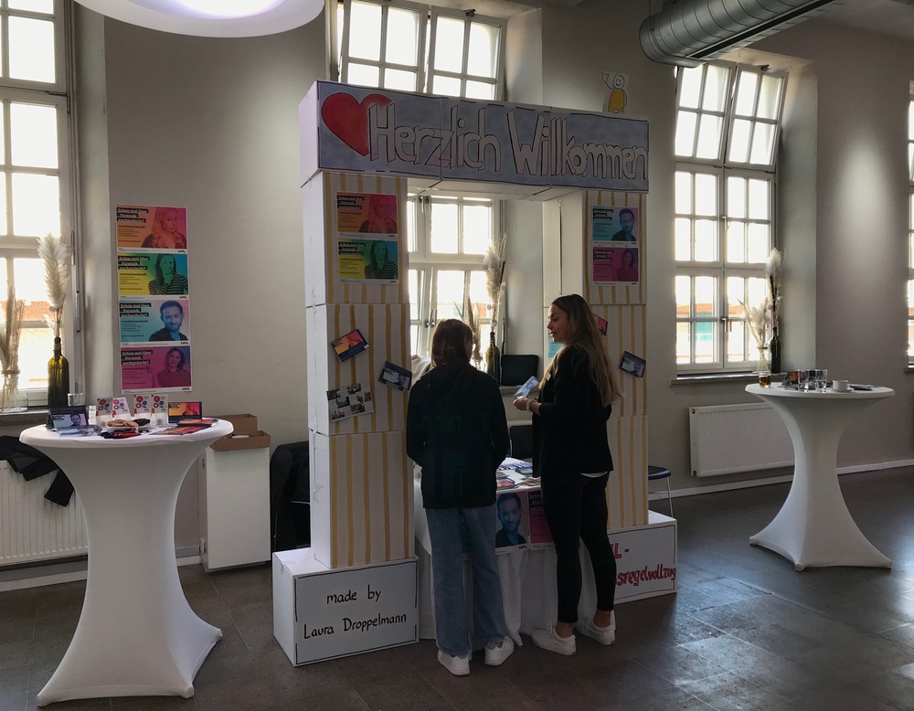 Zwei Frau sprechen miteinander vor einem Infostand. (Bild: LWL/SchuFi)