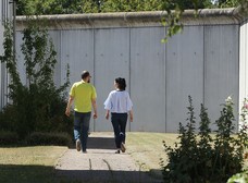 Eine Mitarbeiterin und ein Patient gehen ins Gespräch vertieft über das Klinikgelände entlang der Mauer