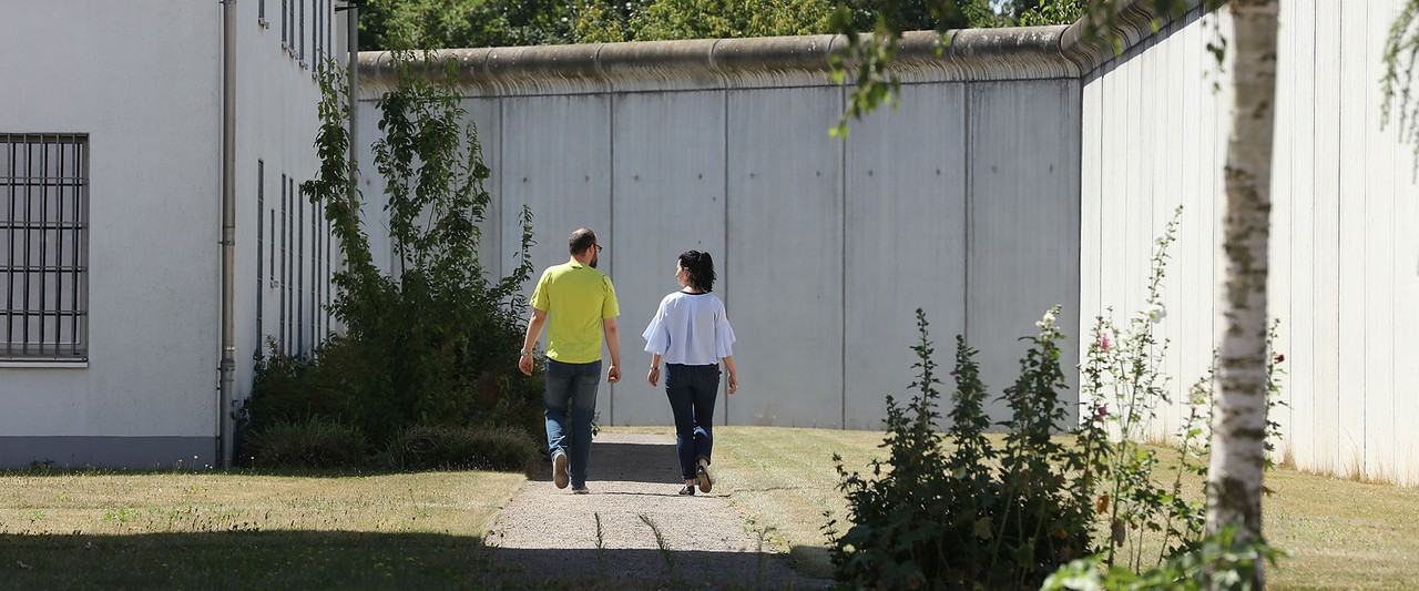 Ein Mann und eine Frau laufen im Gespräch an einer Mauer entlang