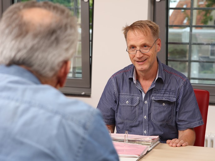 Ein Mann sitzt einem anderen gegenüber und blättert dabei in einer Patientenakte. (Foto: LWL/Wieland)