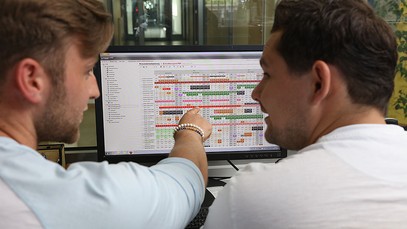 zwei junge Männer beugen sich über einen Bildschirm mit einem Planungsprogramm