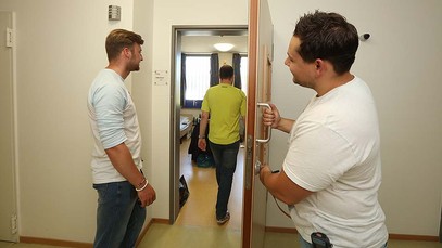Zwei junge Männer begleiten einen dritten Mann in ein Patientenzimmer.