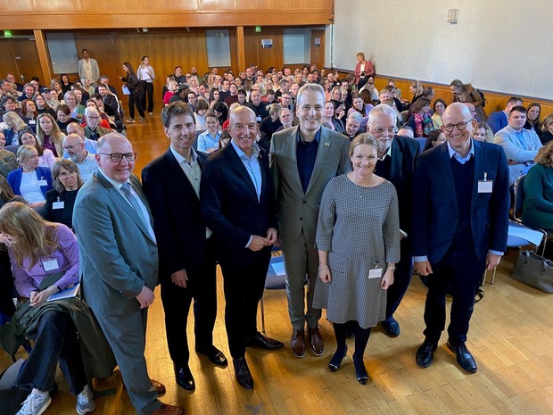 Eine Gruppe von Personen steht mit dem Rücken zu einem voll besetzen Publikumsraum. (Bild: LWL/SchuFi)