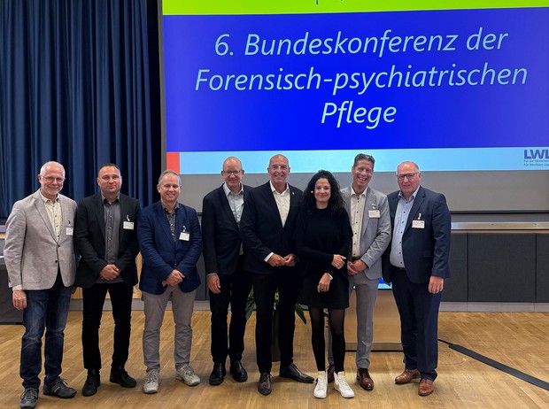 Eine Gruppe von Personen steht vor der Aufschrift "Bundeskonferenz forensisch-psychiatrische Pflege". (Bild: LWL)