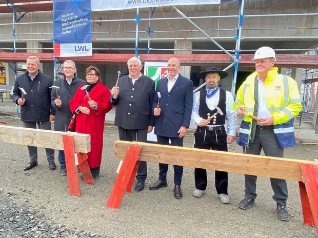 Eine Gruppe von Menschen mit Bauhelmen und Leucht-Schutzwesten steht auf einer Baustelle vor einem großen eingerüsteten Gebäude. (Bild: LWL/SchuFi)